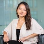 A professional Asian businesswoman sitting confidently in a modern office setting.